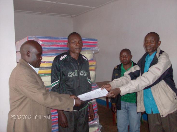 Ezati (left) hands over the invoice in front of the Avari Health Centre Chairperson (centre left) to the nurse in charge (right).